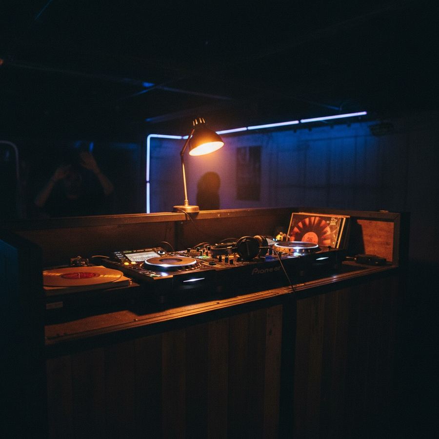 An empty DJ booth with a single warm light illuminating headphones resting on a mixer